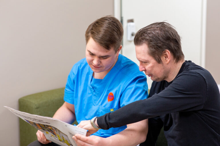 Lähihoitaja lukemassa lehteä asukkaan kanssa